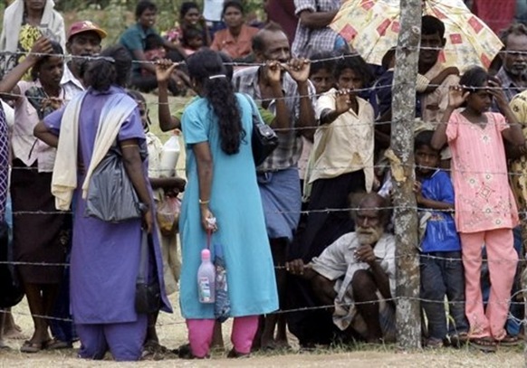 Tamil civilians stand behind a barbed-wire fence in the Manik Farm refugee camp in northern Sri Lanka-eMJPvXSZsA
