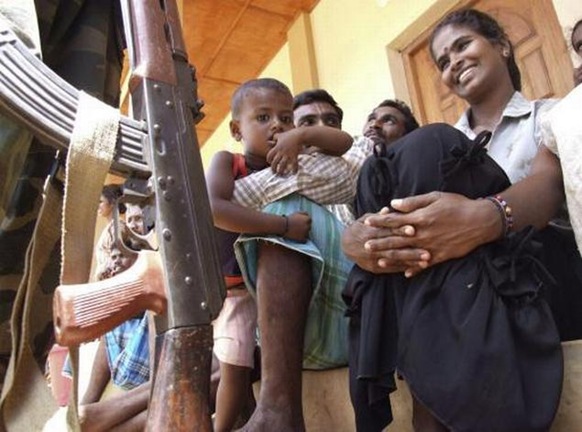 A soldier, left, stands near a Sri Lankan ethnic Tamil family before they were sent back to their village, at a transit camp for displaced civilians in Trincomalee, Sri Lanka, on September 23, 2009 AP