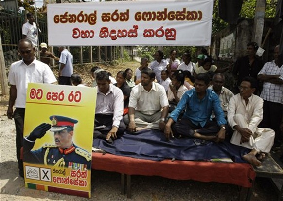 Supporters of defeated Sri Lankan presidential candidate Gen. Sarath Fonseka, seen left on a placard, participate in a sit-in protest demanding his immediate release, in Colombo - ap