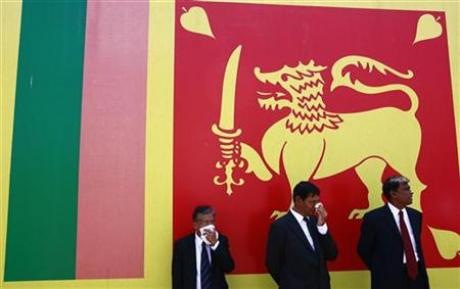 Men cover their faces in front of the national flag as Sri Lankan President Mahinda Rajapaksa's helicopter takes off, at the Yugadanavi Combined Cycle Thermal power plant in the suburb of Kerawalapitiya in Colombo February 25, 2010. Credit: Reuters-Andrew Caballero-Reynolds