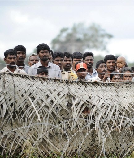 Sri Lankan war-displaced civilians peer from behind barbed wire fences surrounding their internment camp in Vavuniya