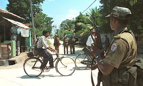 FOR USE WITH "SRI LANKA" -- Sri Lankan police stand guard at a check point as residents travel on  bicycles in Jaffna, Sri Lanka Friday March 5, 1999. There are over 1,000 check points all over the town manned by troops and police, fearing Tamil rebel attacks. Civilian life is far from normal despite attempts by the government to restore civil administration since the town was captured  by government troops in1996 from Tamil rebels. (AP Photo Gemunu Amarasinghe)