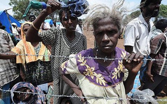  Internally displaced Sri Lankan people wait behind barbed wire at Menik Farm refugee camp in Cheddikulam  Photo: AFP GETTY 