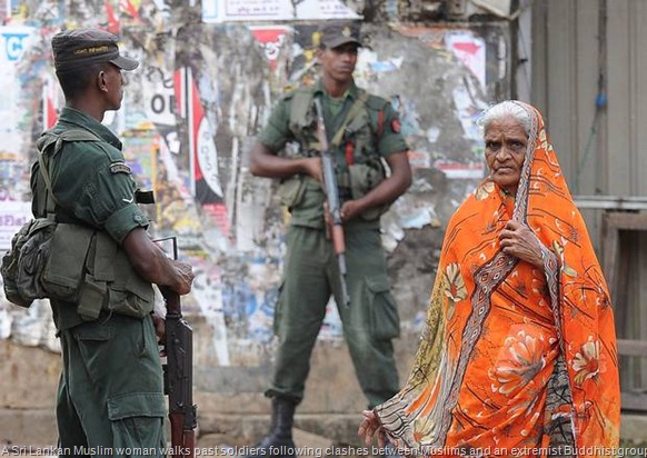 A Sri Lankan Muslim woman walks past soldiers following clashes between Muslims and an extremist Buddhist group in the town of Alutgama on June 17, 2014